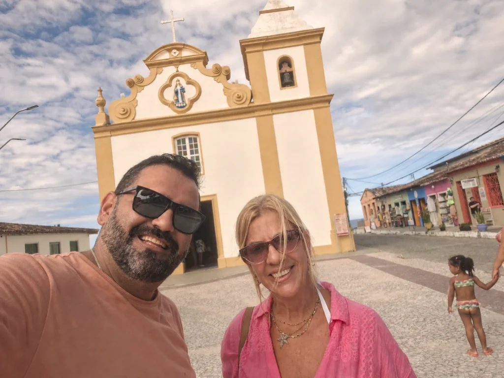 Joaquim e Renata sorrindo em frente a uma igreja durante viagem.