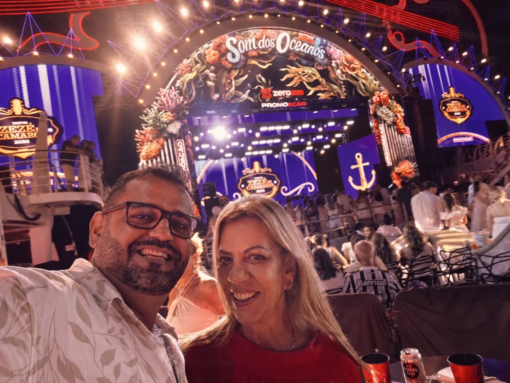 Joaquim e Renata sorrindo em evento musical iluminado.